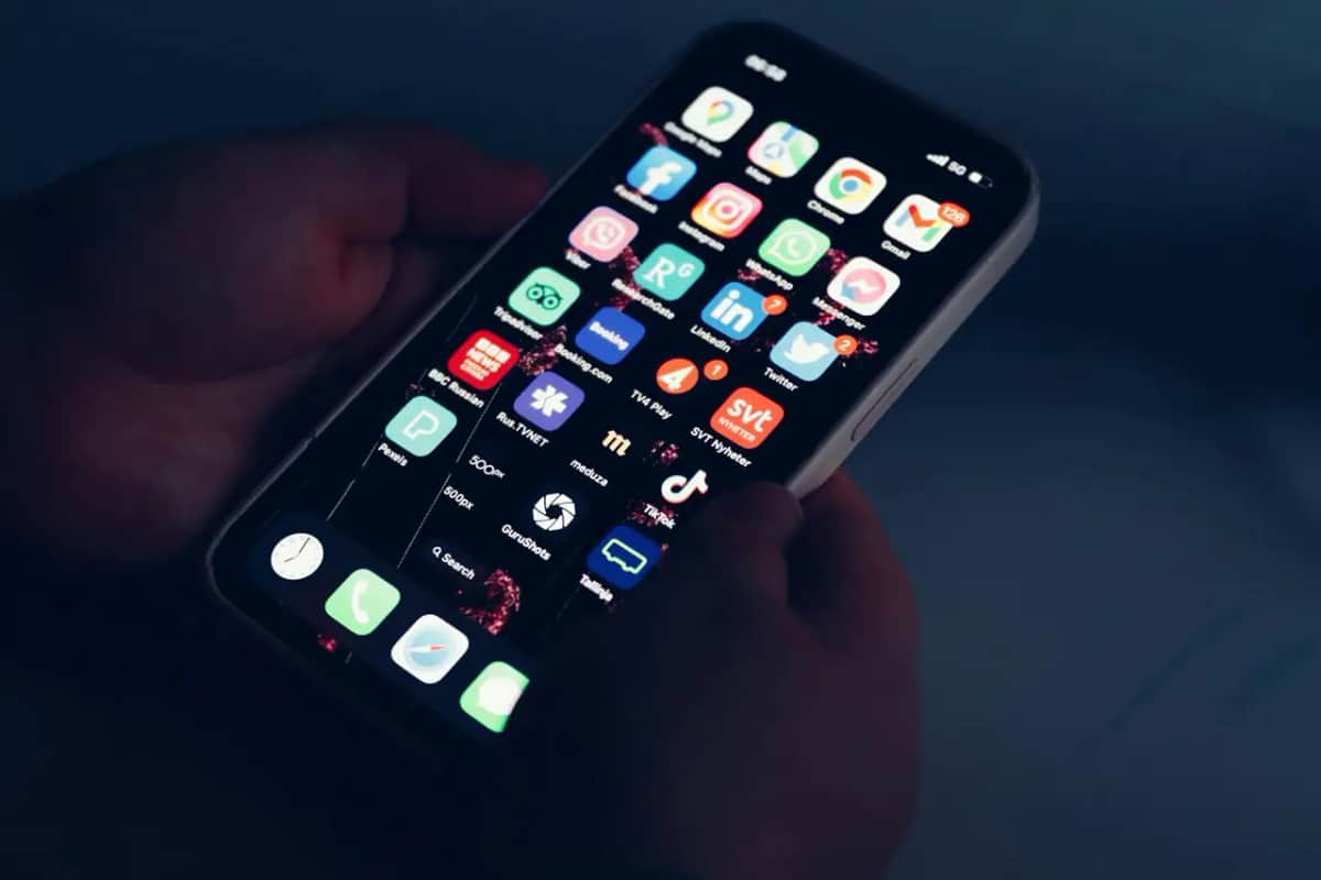 Рука тримає смартфон зі світним екраном і застосунками соцмереж у темряві