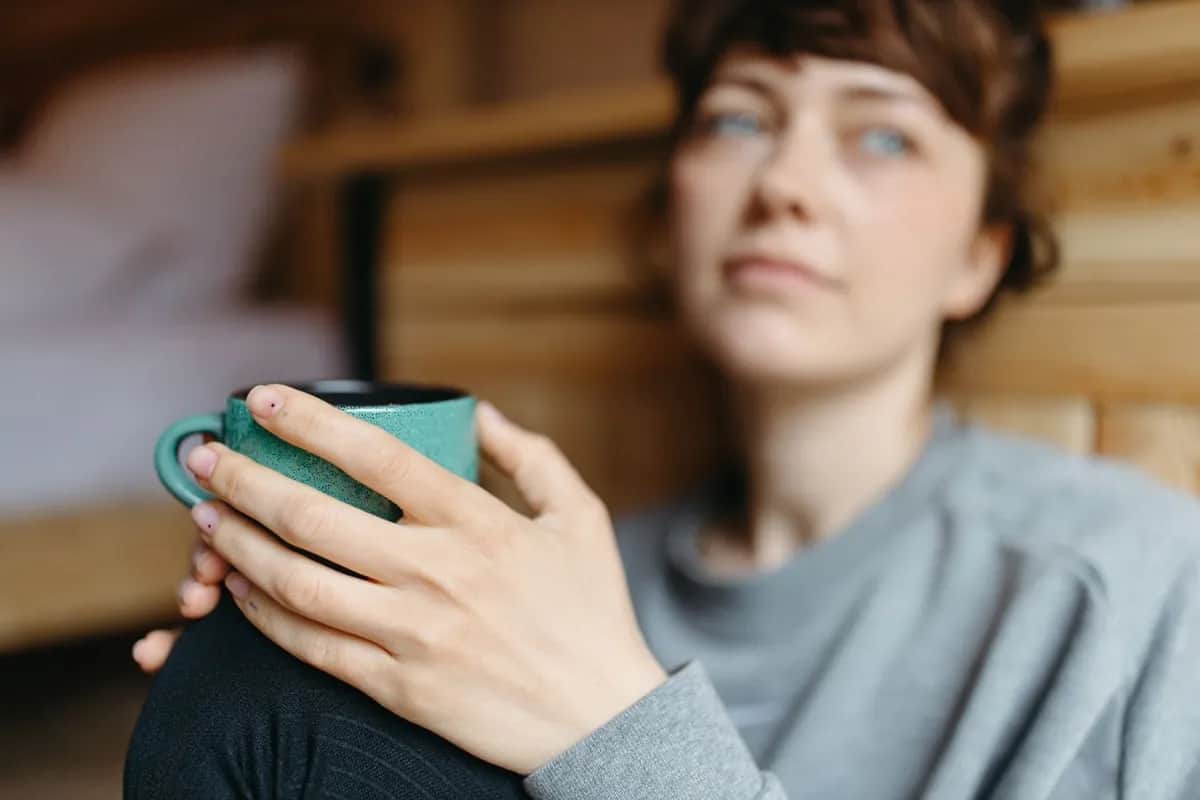 Женщина дома держит чашку, смотрит перед собой с тихой усталостью