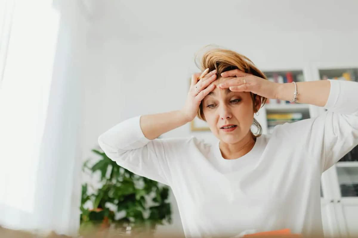 Уставшая женщина держится за голову дома, истощённая от избытка раздражителей