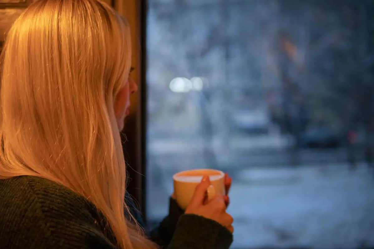 Жінка з теплою чашкою спокійно дивиться у вікно, відчуваючи полегшення після розмови