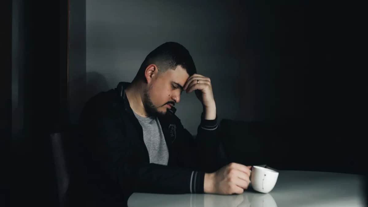Мужчина сидит один за столом в тёмной комнате с чашкой