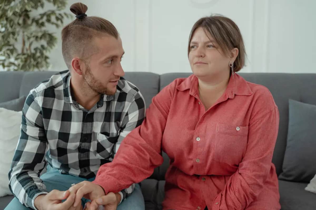 Женщина держит за руку мужчину во время спокойного разговора на диване дома