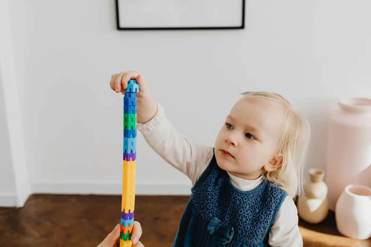 Маленька дитина зосереджено будує вежу з кольорових конструкторів