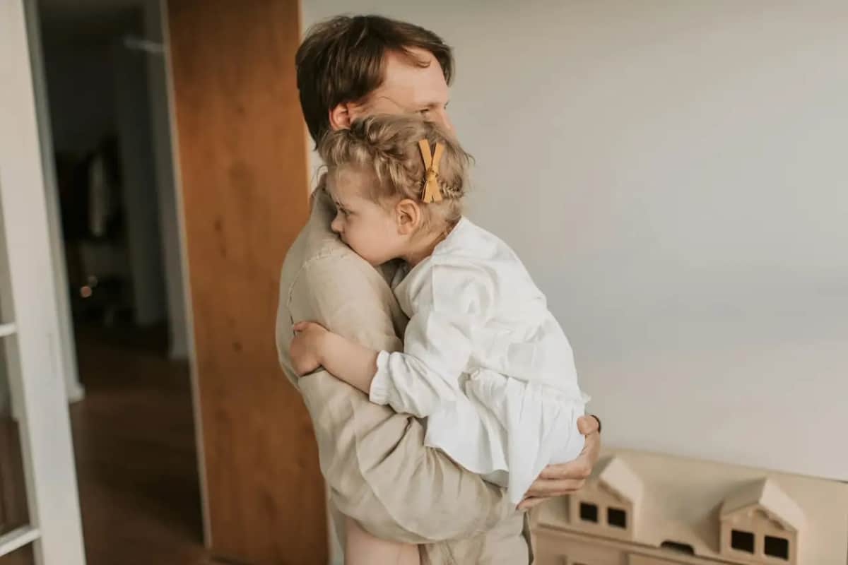 Тато ніжно обіймає й заспокоює маленьку доньку, яка поклала голову йому на плече